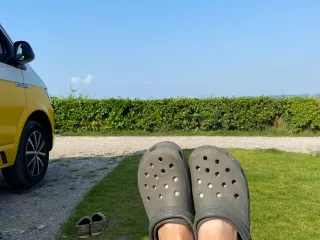 Blick einer Person im Liegestuhl über die eigenen Füße hinweg Richtung einer Hecke.